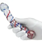 Glass dildo with red and blue swirl design held by a white-gloved hand.